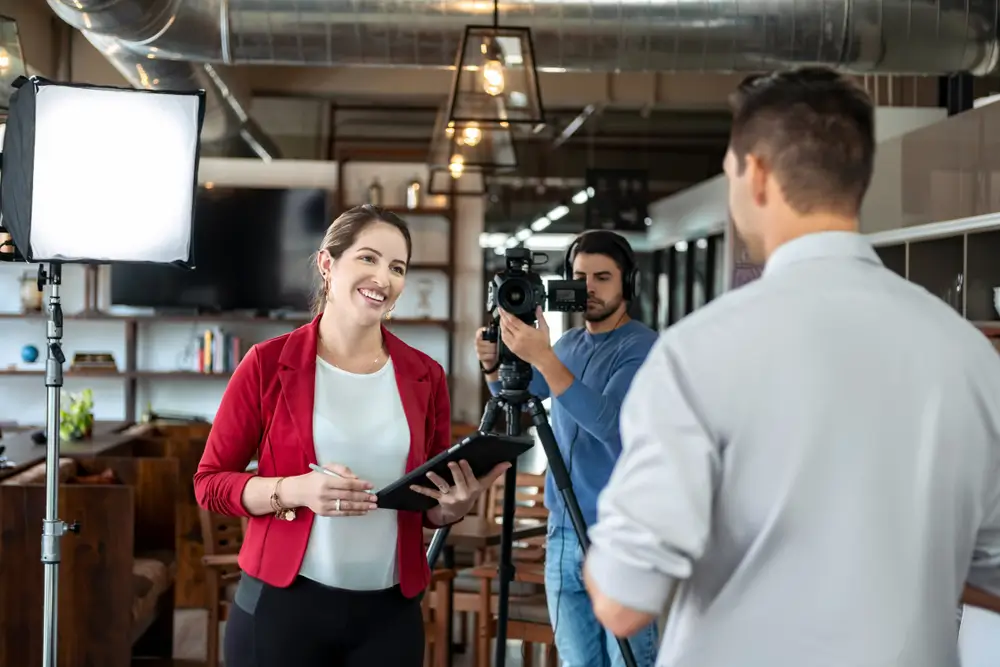 man with camera filming man and woman in a corporate setting